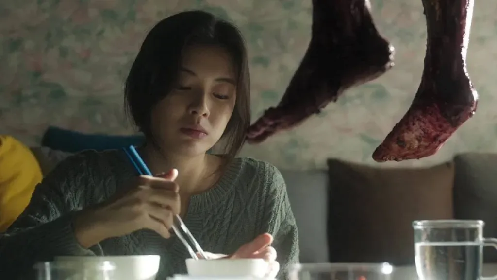 Ruídos | A Criatividade Praticamente Sem Limites do Cinema de Terror Asiático 1 Protagonista de "Ruídos" (2025) durante refeição, com vista do pé de uma pessoa ensanguentada, pendurada.