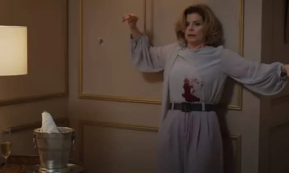 Cena da morte de Odete Roitman no remake de 2025 de "Vale Tudo", com Débora Bloch com o icônico vestido do original e deslizando na parede com a barriga ensanguentada.