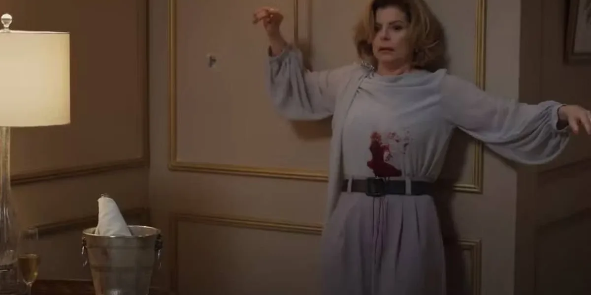 Cena da morte de Odete Roitman no remake de 2025 de "Vale Tudo", com Débora Bloch com o icônico vestido do original e deslizando na parede com a barriga ensanguentada.