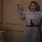 Cena da morte de Odete Roitman no remake de 2025 de "Vale Tudo", com Débora Bloch com o icônico vestido do original e deslizando na parede com a barriga ensanguentada.