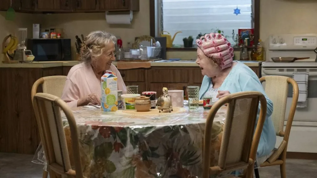 Eleanor e sua amiga no filme "A Incrível Eleanor", sentadas à mesa, compartilhando um café da tarde.