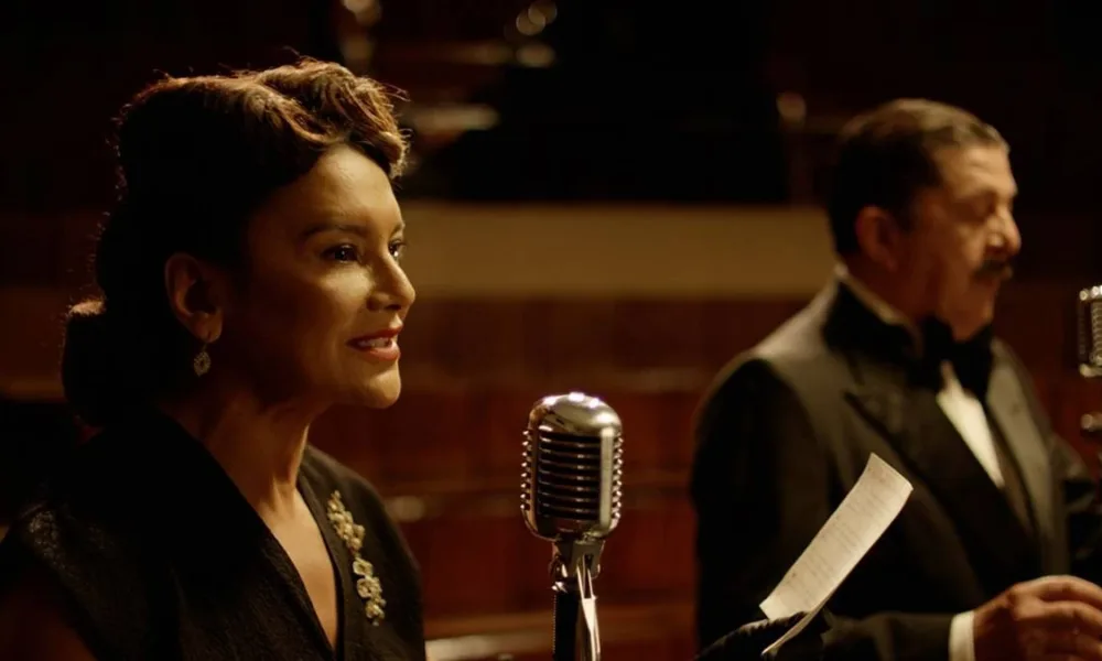 Imagem do filme "Ary", biografia de Ary Barroso, com destaque na foto para personagem retratada por Dira Paes à esquerda em frente a microfone.