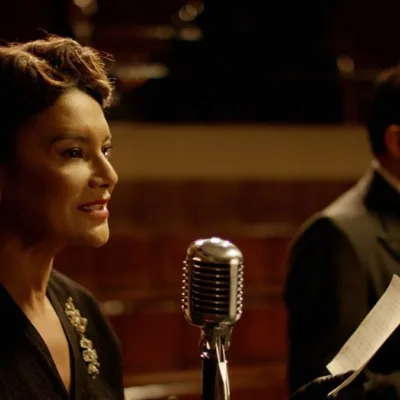 Imagem do filme "Ary", biografia de Ary Barroso, com destaque na foto para personagem retratada por Dira Paes à esquerda em frente a microfone.