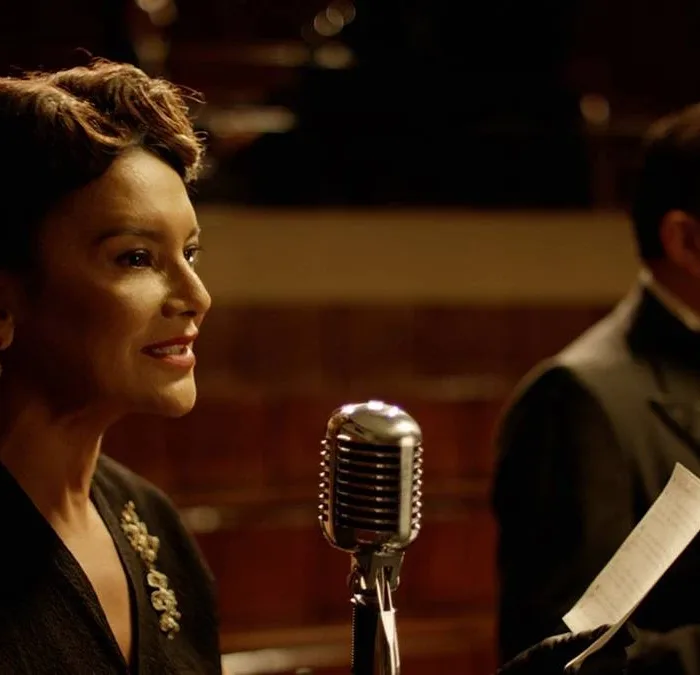 Imagem do filme "Ary", biografia de Ary Barroso, com destaque na foto para personagem retratada por Dira Paes à esquerda em frente a microfone.