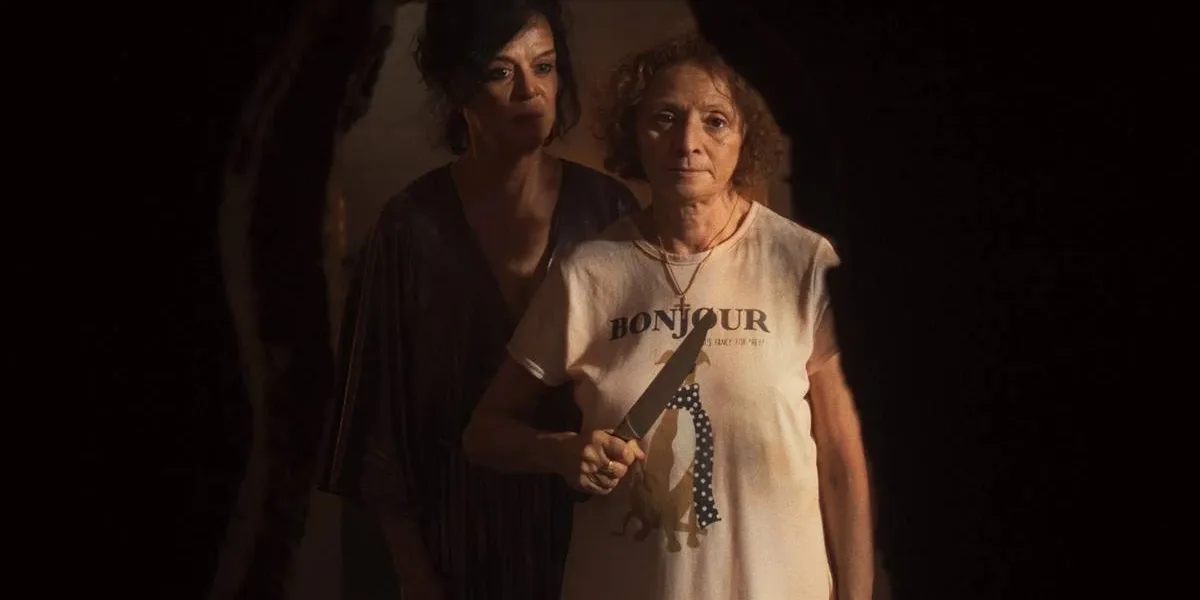 Gravidade | Às Vezes É No Fim de Tudo Que Nos Encontramos Imagem promocional do filme "Gravidade" (2025). Uma mulher à frente segura uma faca na altura do peito, enquanto outra está atrás dela, olhando para o mesmo ponto que ela, nosso ponto de vista de câmera.