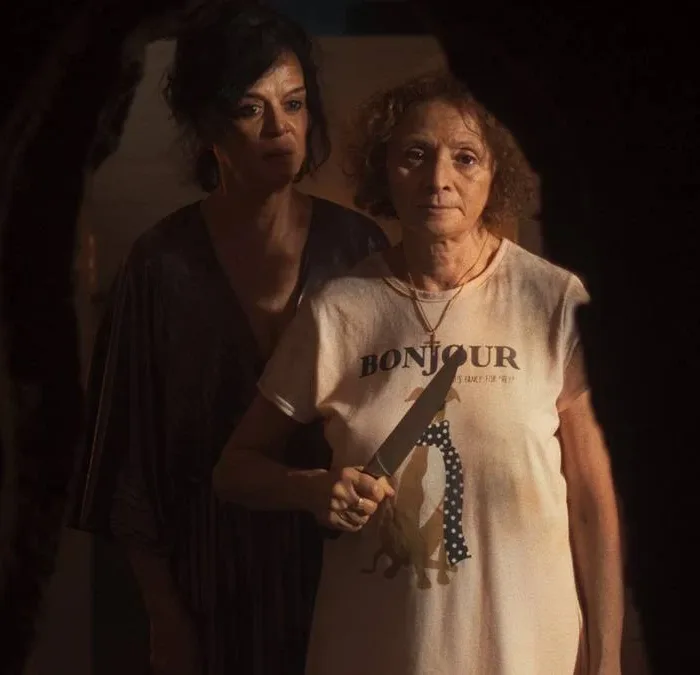 Imagem promocional do filme "Gravidade" (2025). Uma mulher à frente segura uma faca na altura do peito, enquanto outra está atrás dela, olhando para o mesmo ponto que ela, nosso ponto de vista de câmera.