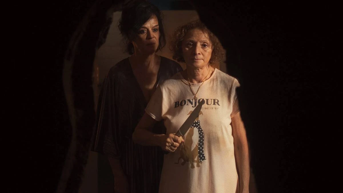 Gravidade | Às Vezes É No Fim de Tudo Que Nos Encontramos 2 Imagem promocional do filme "Gravidade" (2025). Uma mulher à frente segura uma faca na altura do peito, enquanto outra está atrás dela, olhando para o mesmo ponto que ela, nosso ponto de vista de câmera.