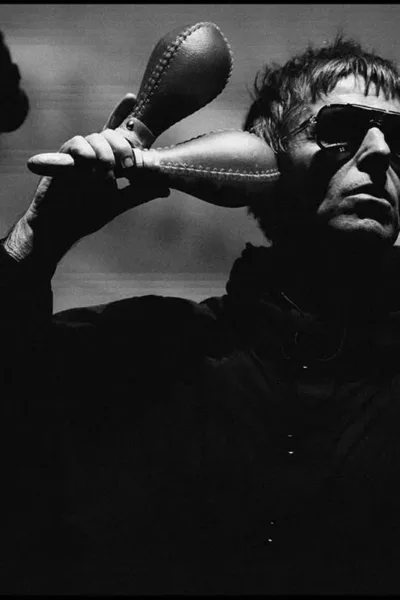 Liam Gallagher em show do Oasis na turnê de reunião de 2025, em Sidney, dia 7 de novembro, de jaqueta e óculos escuros, segurando duas maracas. Foto em preto e branco.