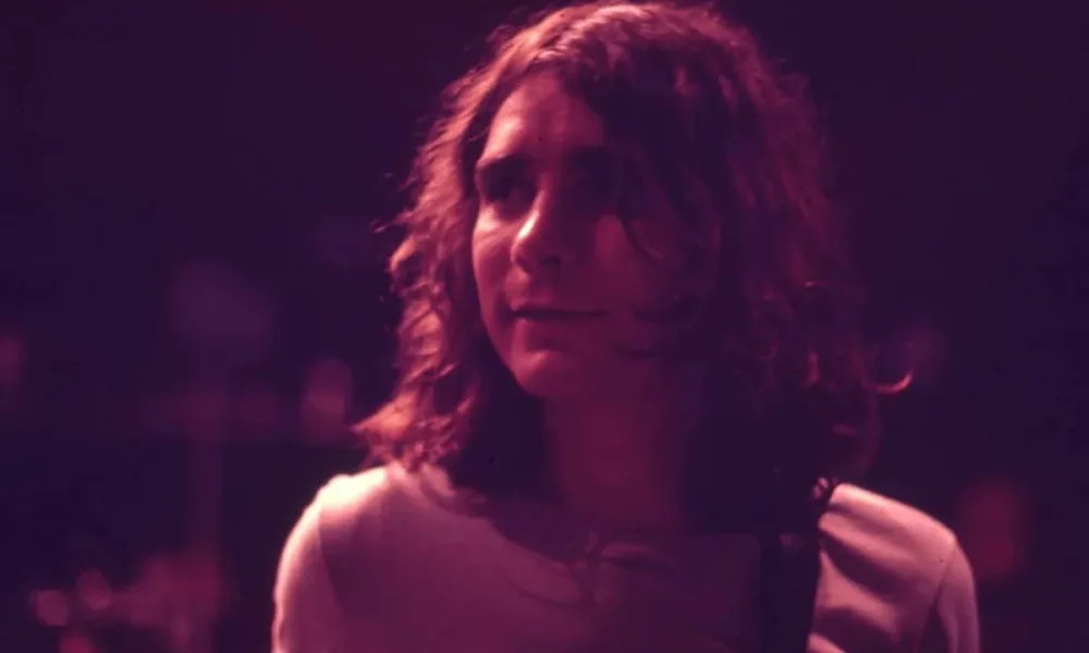 Fotografia em filtro vermelho arroxeado de Lô Borges na juventude.