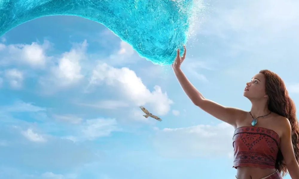 Catherine Laga‘aia como Moana no live action de 2026. Ela está no canto inferior direito tocando o mar que se move até ela como um tentáculo brilhante, ocupando a maior parte da tela.