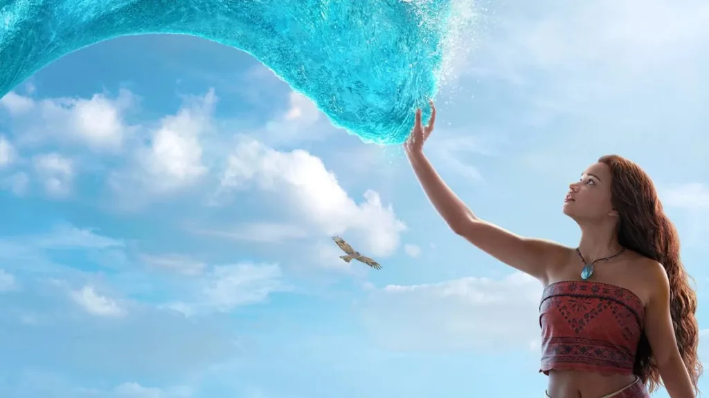 Catherine Laga‘aia como Moana no live action de 2026. Ela está no canto inferior direito tocando o mar que se move até ela como um tentáculo brilhante, ocupando a maior parte da tela.