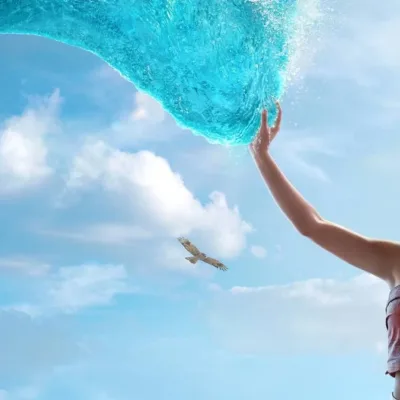 Catherine Laga‘aia como Moana no live action de 2026. Ela está no canto inferior direito tocando o mar que se move até ela como um tentáculo brilhante, ocupando a maior parte da tela.