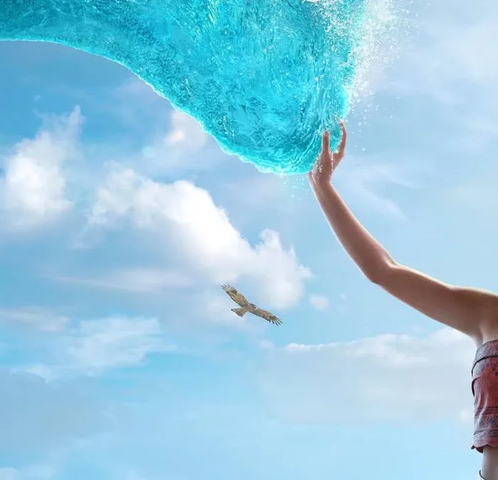 Catherine Laga‘aia como Moana no live action de 2026. Ela está no canto inferior direito tocando o mar que se move até ela como um tentáculo brilhante, ocupando a maior parte da tela.