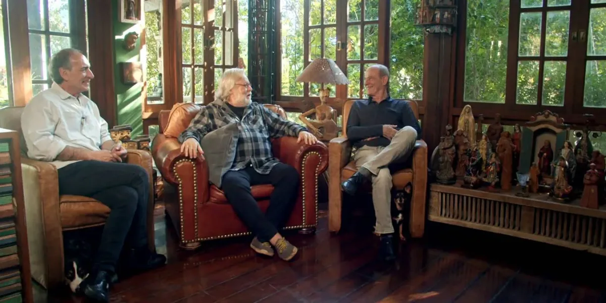 Gérson Conrad, Willy Verdaguer, Ney Matogrosso, cada um em uma poltrona, conversando e rindo durante filmagem do documentário "Primavera nos Dentes: a História dos Secos & Molhados".