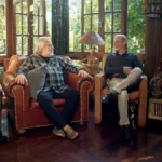 Gérson Conrad, Willy Verdaguer, Ney Matogrosso, cada um em uma poltrona, conversando e rindo durante filmagem do documentário "Primavera nos Dentes: a História dos Secos & Molhados".