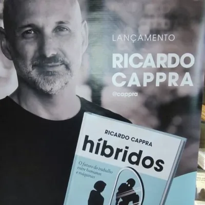 Pôster com autor Ricardo Cappra em matiz sépia segurando livro "Híbridos" em lançamento.