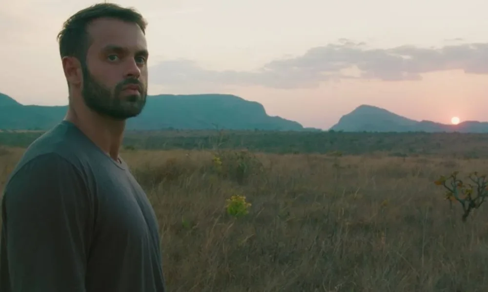 Capa do filme "Ser Feliz Por Nenhum Motivo", com um homem em uma paisagem de planície no pôr-do-sol.