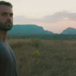 Capa do filme "Ser Feliz Por Nenhum Motivo", com um homem em uma paisagem de planície no pôr-do-sol.