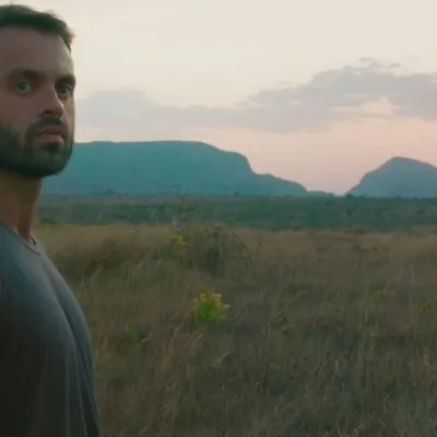 Capa do filme "Ser Feliz Por Nenhum Motivo", com um homem em uma paisagem de planície no pôr-do-sol.