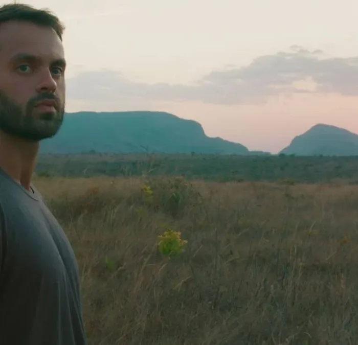 Capa do filme "Ser Feliz Por Nenhum Motivo", com um homem em uma paisagem de planície no pôr-do-sol.