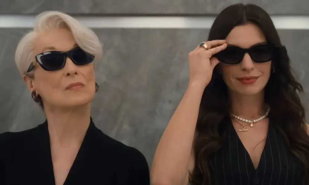 Meryl Streep (esquerda) e Anne Hathaway (direita) em elevador de óculos escuros reprisando os papéis de Miranda e Andy na continuação "O Diabo Veste Prada 2". Ambas estão de preto e câmera as pega do busto para cima.