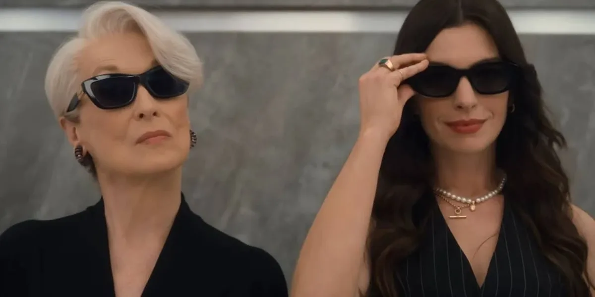 Meryl Streep (esquerda) e Anne Hathaway (direita) em elevador de óculos escuros reprisando os papéis de Miranda e Andy na continuação "O Diabo Veste Prada 2". Ambas estão de preto e câmera as pega do busto para cima.