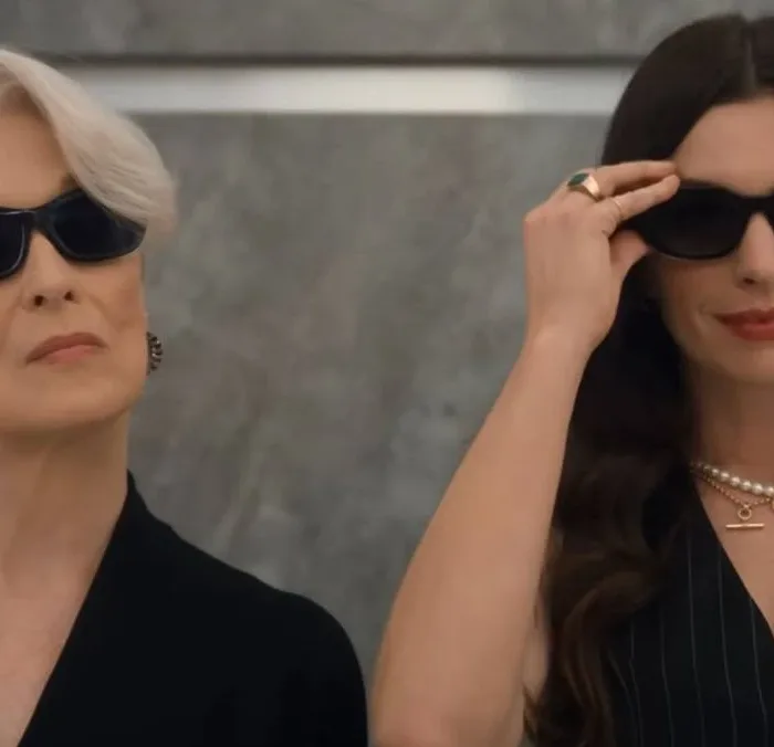 Meryl Streep (esquerda) e Anne Hathaway (direita) em elevador de óculos escuros reprisando os papéis de Miranda e Andy na continuação "O Diabo Veste Prada 2". Ambas estão de preto e câmera as pega do busto para cima.