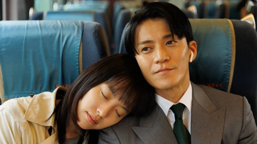 Han Hyo-joo como Lee Hana (esquerda) e Shun Oguri como Sosuke Fujiwara (direita), ela recostada no ombro dele em viagem de ônibus na série "Românticos Anônimos".