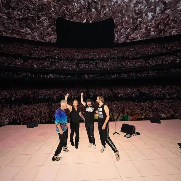 Membros do U2 em show Live at Sphere em 2024, de costas para o palco, tirando foto com o público.