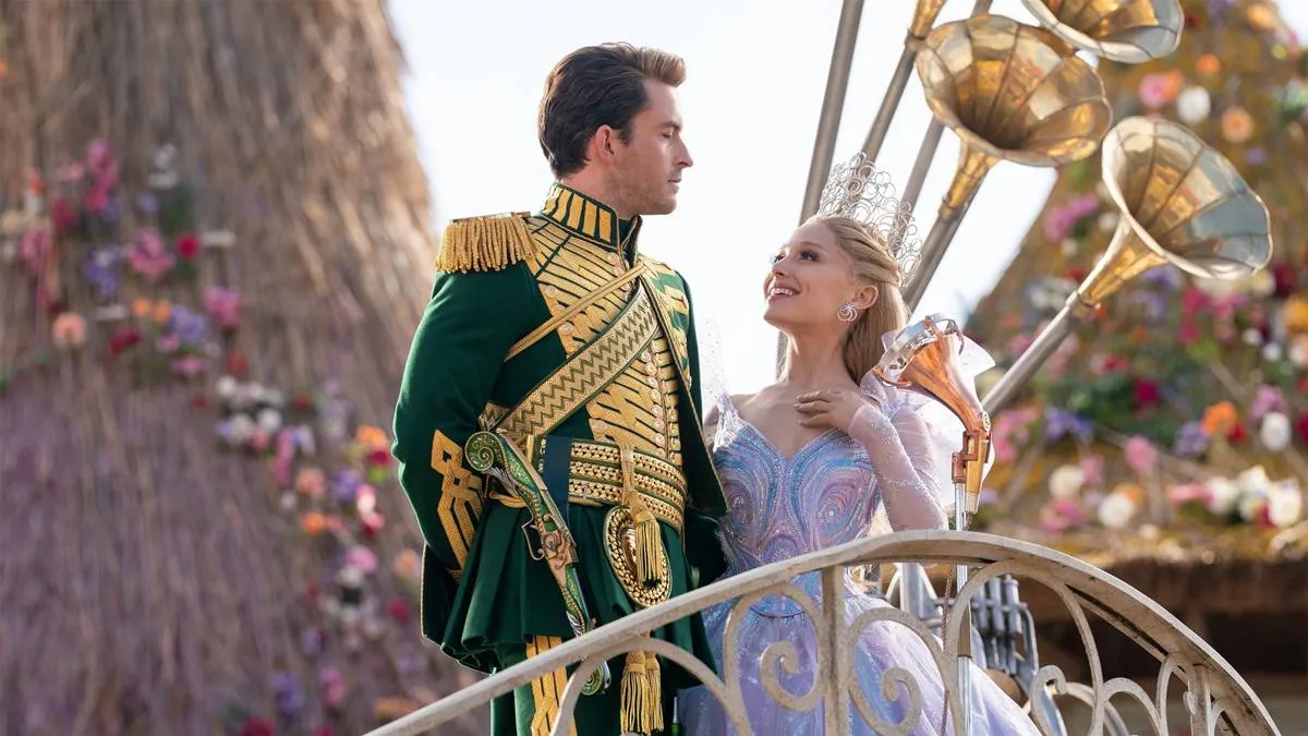 Jonathan Bailey (esquerda) e Ariana Grande (direita) como Fiyero e Glinda na segunda parte de "Wicked" (2025). Eles estão num cortejo em Oz, na frente de um boneco de vime ao fundo. Eles se olham.