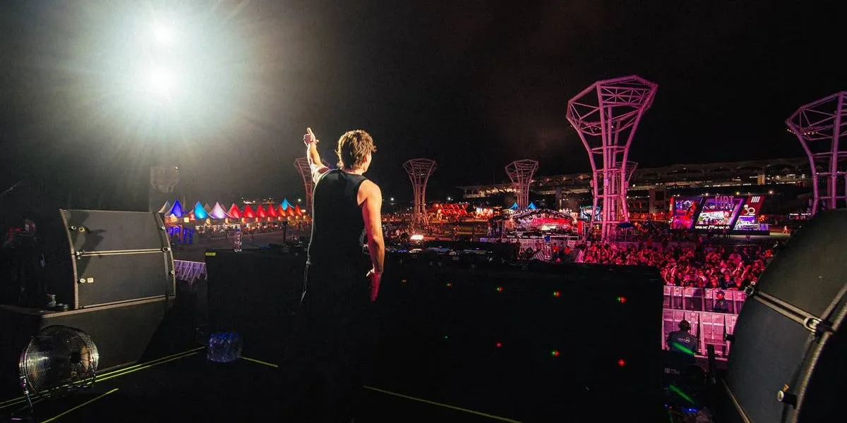 Bunt em fotografia tirada de costas com artista acenando para plateia no palco Perry's do Lollapalooza 2026.