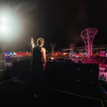 Bunt em fotografia tirada de costas com artista acenando para plateia no palco Perry's do Lollapalooza 2026.