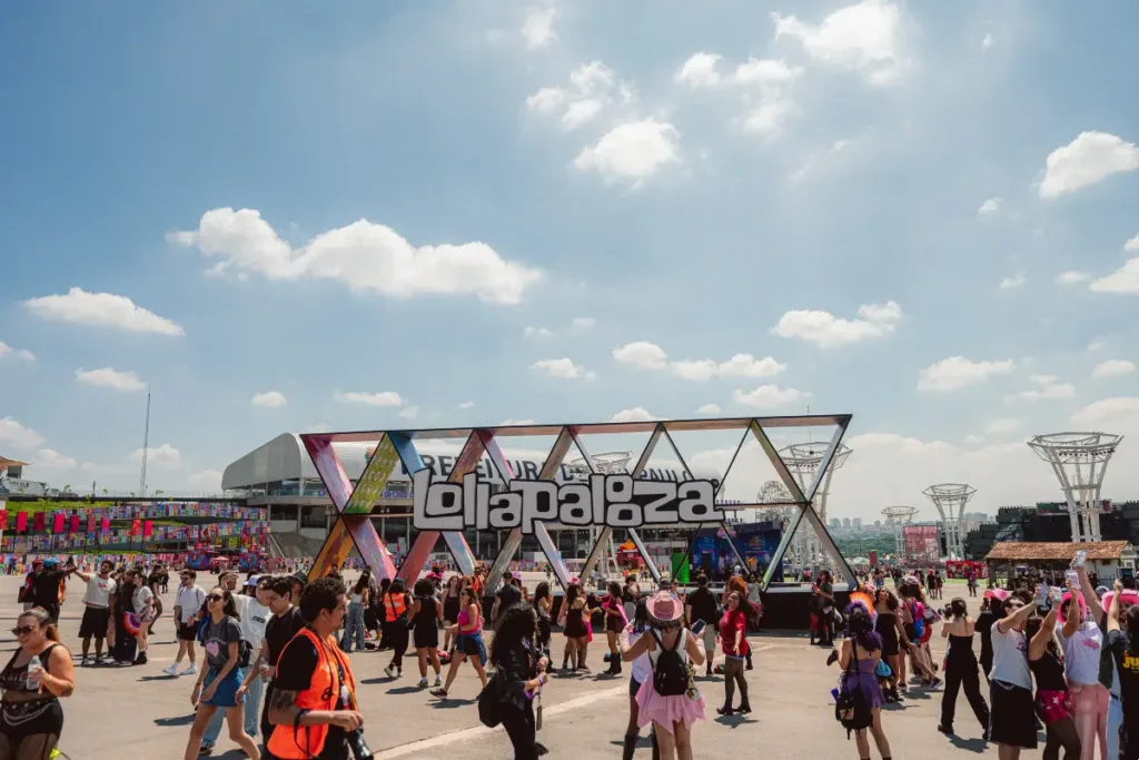 Estrutura de escultura com o logo do Lollapalooza com público passando pela praça no sábado do evento em 2026.