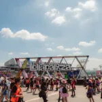 Estrutura de escultura com o logo do Lollapalooza com público passando pela praça no sábado do evento em 2026.