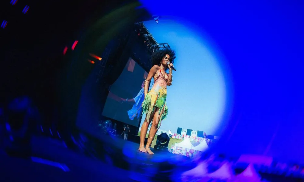 Captura de tela através de lente azul focando em Agnes Nunes durante seu show no Lollapalooza 2026. Cantoar está usando um vestido com top e saia verde.
