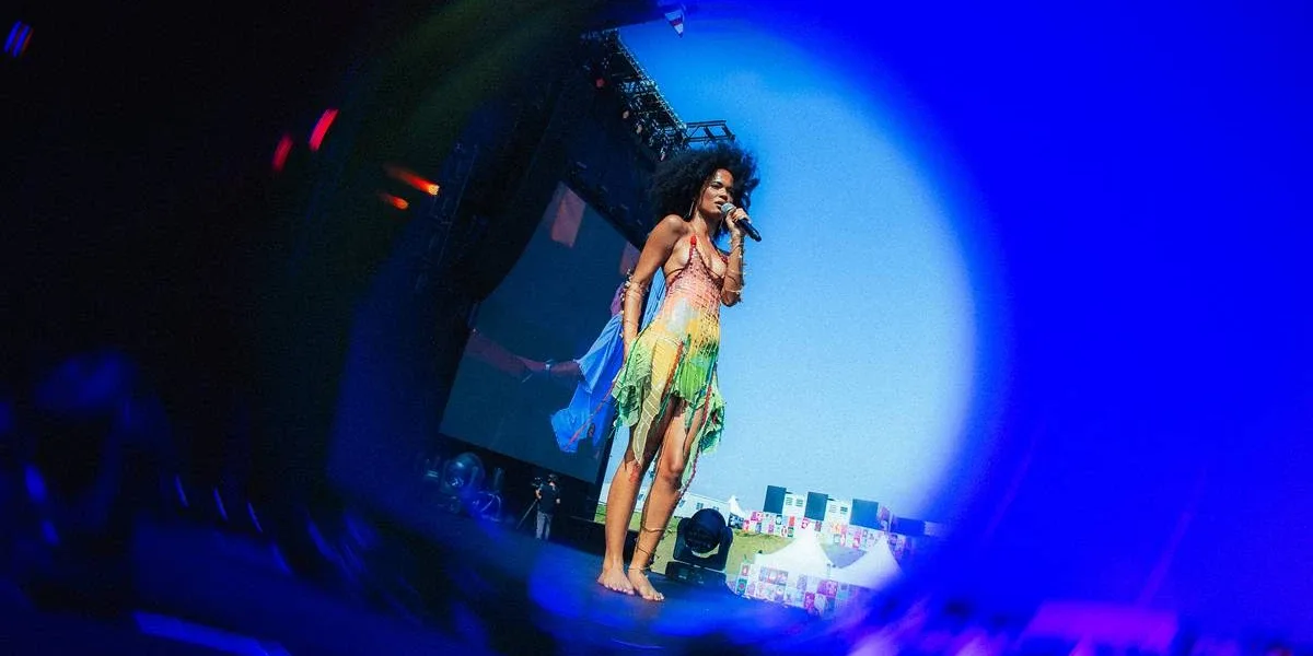 Lollapalooza 2026 | Agnes Nunes Traz Encontro de Gerações em Show de Destaque Captura de tela através de lente azul focando em Agnes Nunes durante seu show no Lollapalooza 2026. Cantoar está usando um vestido com top e saia verde.