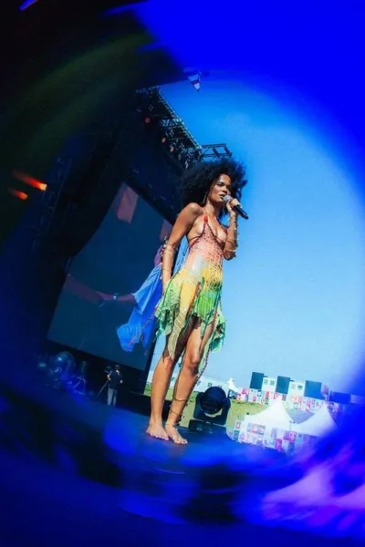 Captura de tela através de lente azul focando em Agnes Nunes durante seu show no Lollapalooza 2026. Cantoar está usando um vestido com top e saia verde.