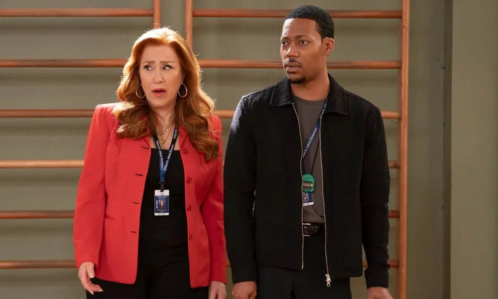 Lisa Ann Walter e Tyler James Williams como os personagens Melissa Schemmenti e Gregory Eddie no 14ª episódio da 5ª temporada de "Abbott Elementary". Eles estão no ginásio do colégio, há uma parede de alongamento ao fundo, e fazem uma cara de surpresa olhando à esquerda.