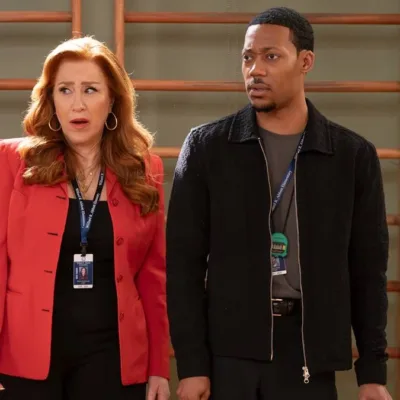 Lisa Ann Walter e Tyler James Williams como os personagens Melissa Schemmenti e Gregory Eddie no 14ª episódio da 5ª temporada de "Abbott Elementary". Eles estão no ginásio do colégio, há uma parede de alongamento ao fundo, e fazem uma cara de surpresa olhando à esquerda.