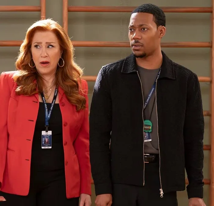 Lisa Ann Walter e Tyler James Williams como os personagens Melissa Schemmenti e Gregory Eddie no 14ª episódio da 5ª temporada de "Abbott Elementary". Eles estão no ginásio do colégio, há uma parede de alongamento ao fundo, e fazem uma cara de surpresa olhando à esquerda.