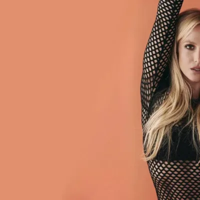 Britney Spears à direita da tela com braços erguidos em dança, encarando a câmera, em parede de fundo salmão em ensaio para o documentário "Britney: No Filter".