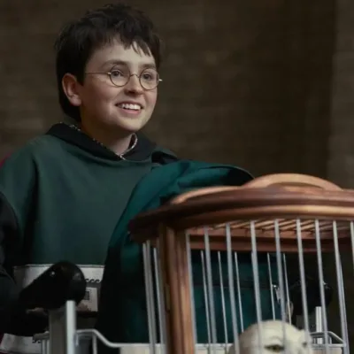 Dominic McLaughlin no primeiro trailer da série de "Harry Potter", da HBO. Ator mirim está vestido de verde, com luvas, e empurra um carrinho com seus pertences, sorrindo, na plataforma 9 3/4.