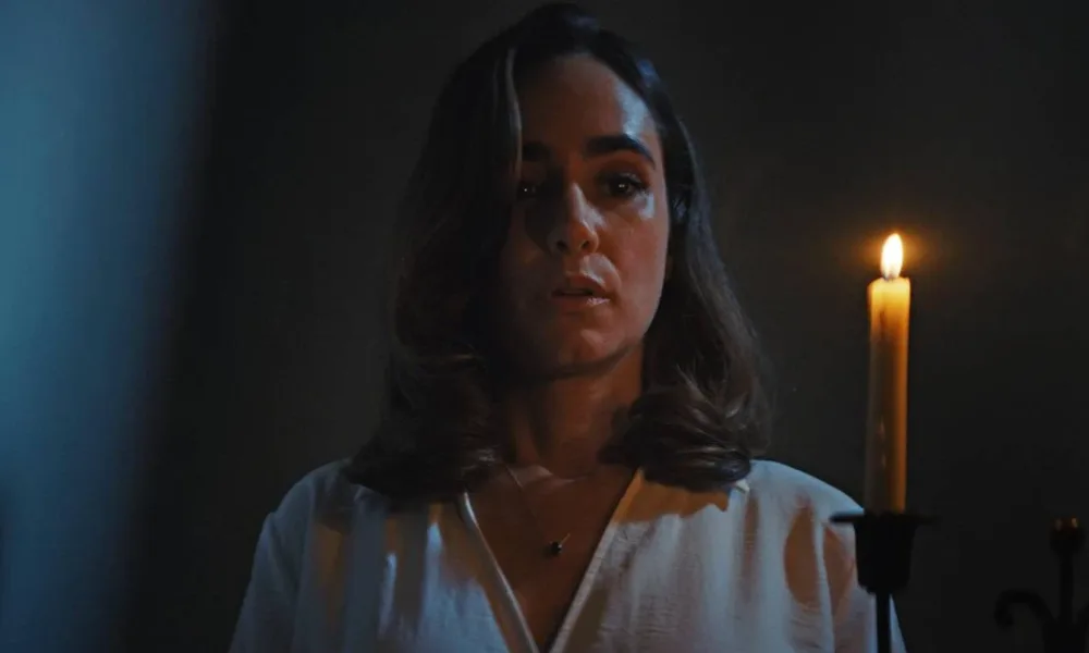 Alicia Sanz como a protagonista Natalie Flores em 'Push: no Limite do Medo', em cena do filme tensa segurando uma vela com a mão esquerda (à nossa direita) iluminando seu rosto no escuro.