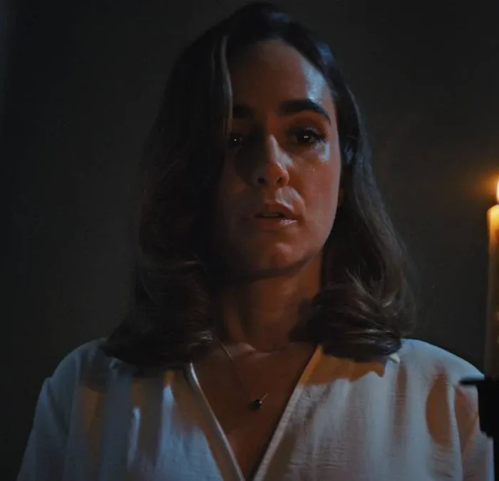 Alicia Sanz como a protagonista Natalie Flores em 'Push: no Limite do Medo', em cena do filme tensa segurando uma vela com a mão esquerda (à nossa direita) iluminando seu rosto no escuro.