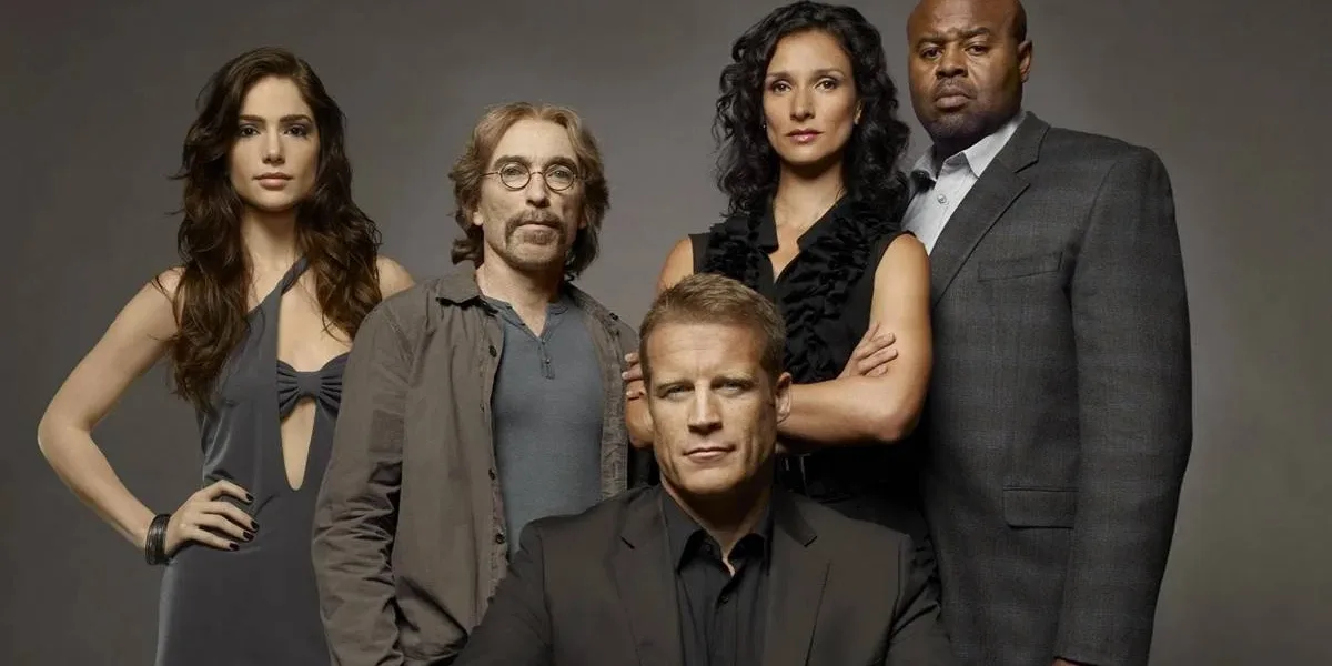 Elenco de "Screener: Alvo Humano" com protagonista ao centor centado, enquanto o resto do elenco está em pé posando para foto promocional em fundo cinza caracterizados como seus personagens na série.