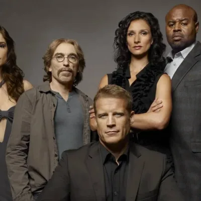 Elenco de "Screener: Alvo Humano" com protagonista ao centor centado, enquanto o resto do elenco está em pé posando para foto promocional em fundo cinza caracterizados como seus personagens na série.