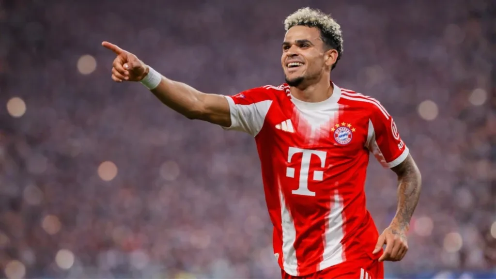 Bayern Vira nos Acréscimos, Elimina o Real Madrid e Avança à Semifinal da Champions 2 Jogador Luis Díaz com uniforme do Bayern, braço direito levantado em comemoração a um gol. Jogo do dia 15/04/2026. Imagem gerada por IA.