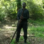 Sterling K. Brown como Xavier Collins na temporada 2, episódio 2, de "Paradise". Ele está com roupas de treinamento, centralizado na foto, no meio de uma floresta, segurando um grande galho.