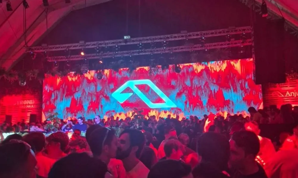 Foto do primeiro Anjuna Deep Open Air em São Paulo, 2026. Luzes vermelhas no ambiente, telão ao fundo, público aglomerado.