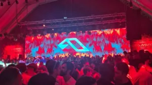 Foto do primeiro Anjuna Deep Open Air em São Paulo, 2026. Luzes vermelhas no ambiente, telão ao fundo, público aglomerado.
